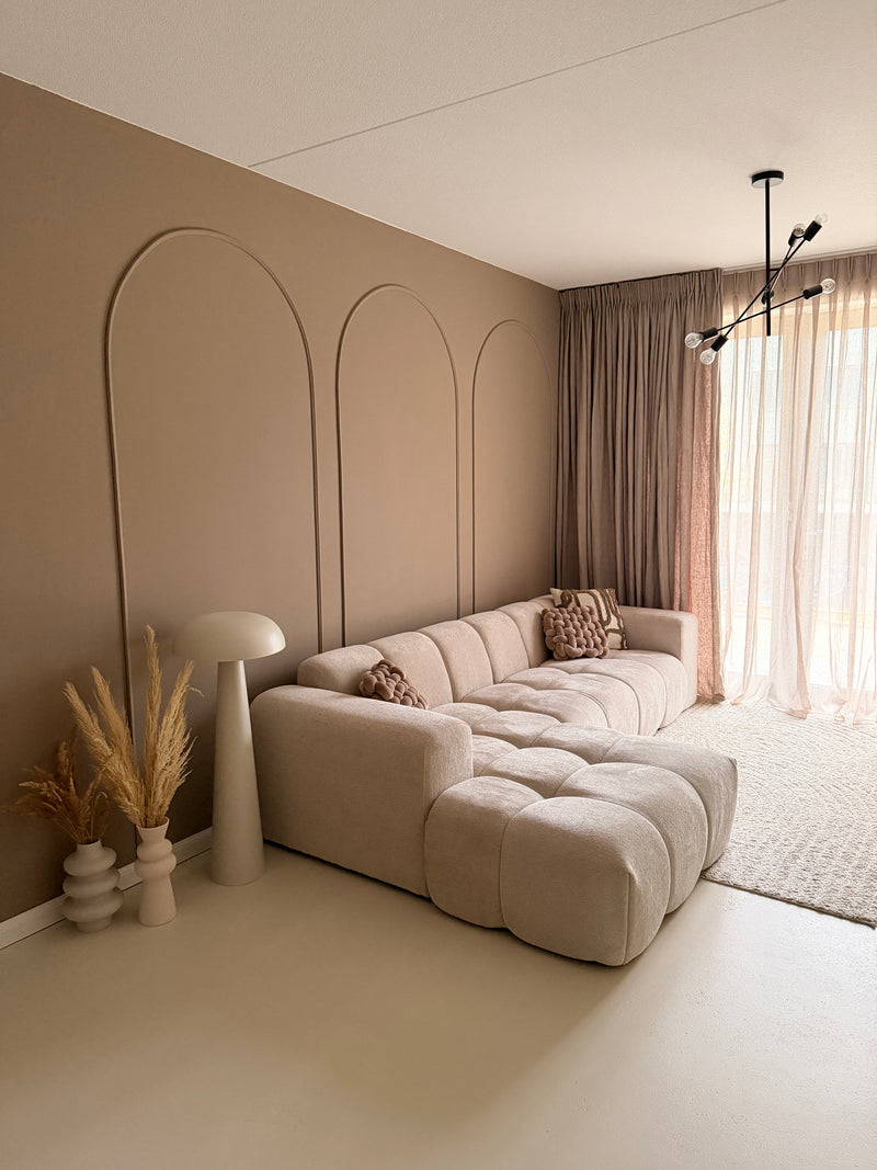 Japandi interieurstijl met taupe muren en wandpanelen gemaakt van flexibele sierlijsten, gecombineerd met een beige bank en zwarte hanglamp.