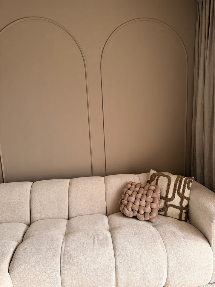 Close-up van een beige bank met sierkussens, met op de achtergrond subtiele wanddecoratie gecreëerd met Velida flexlijsten